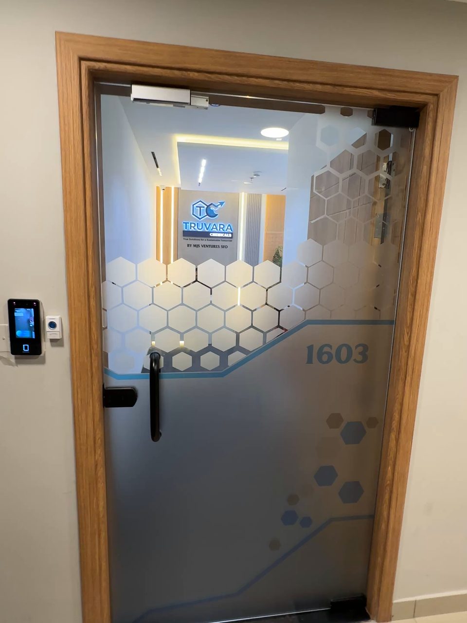 After: frosted glass entrance door with hexagon manifestation, opening onto a lit reception